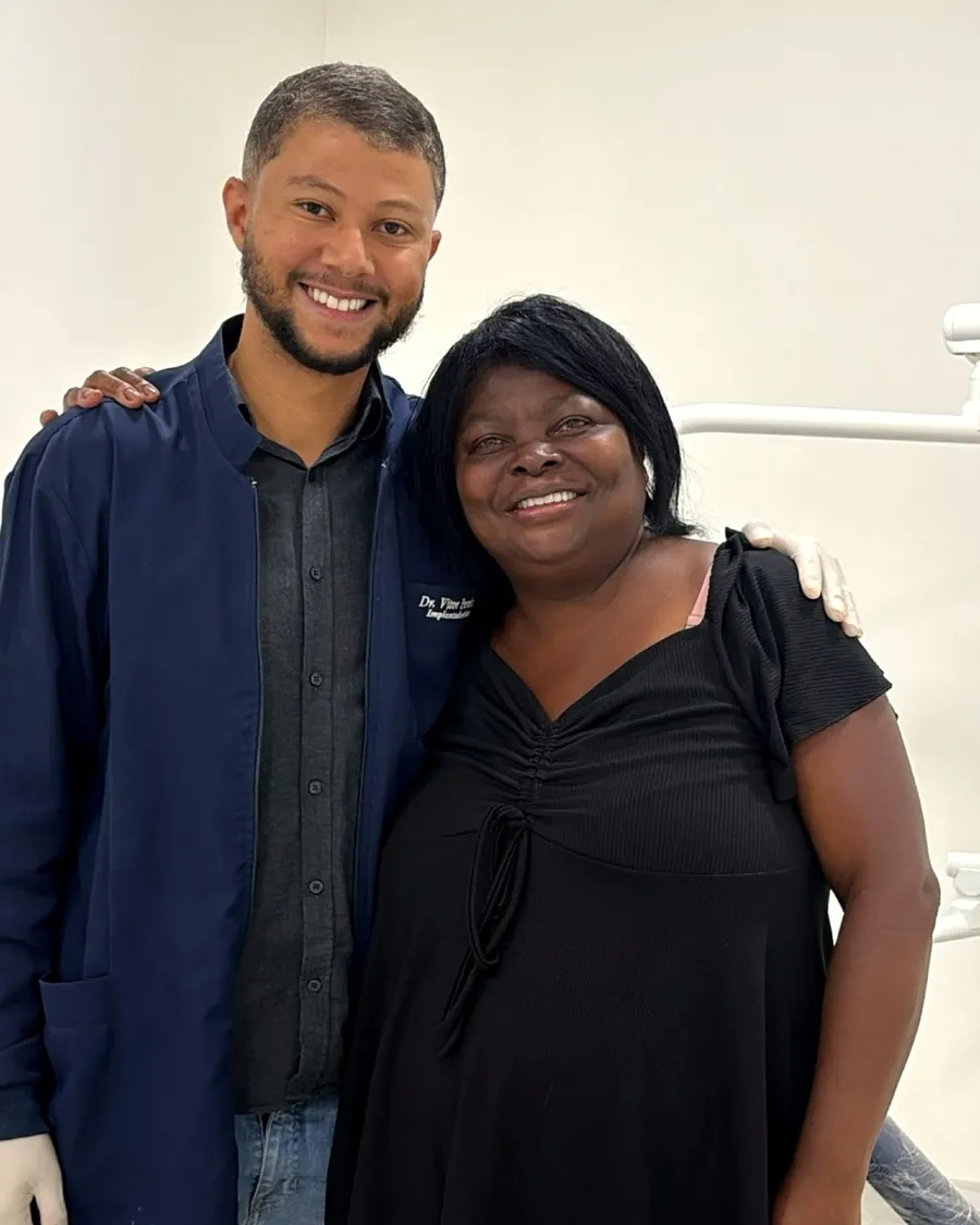 Dona Jucimar sorrindo ao lado do Dr. Vitor Pereira no consultório da Sorria Nepomuceno